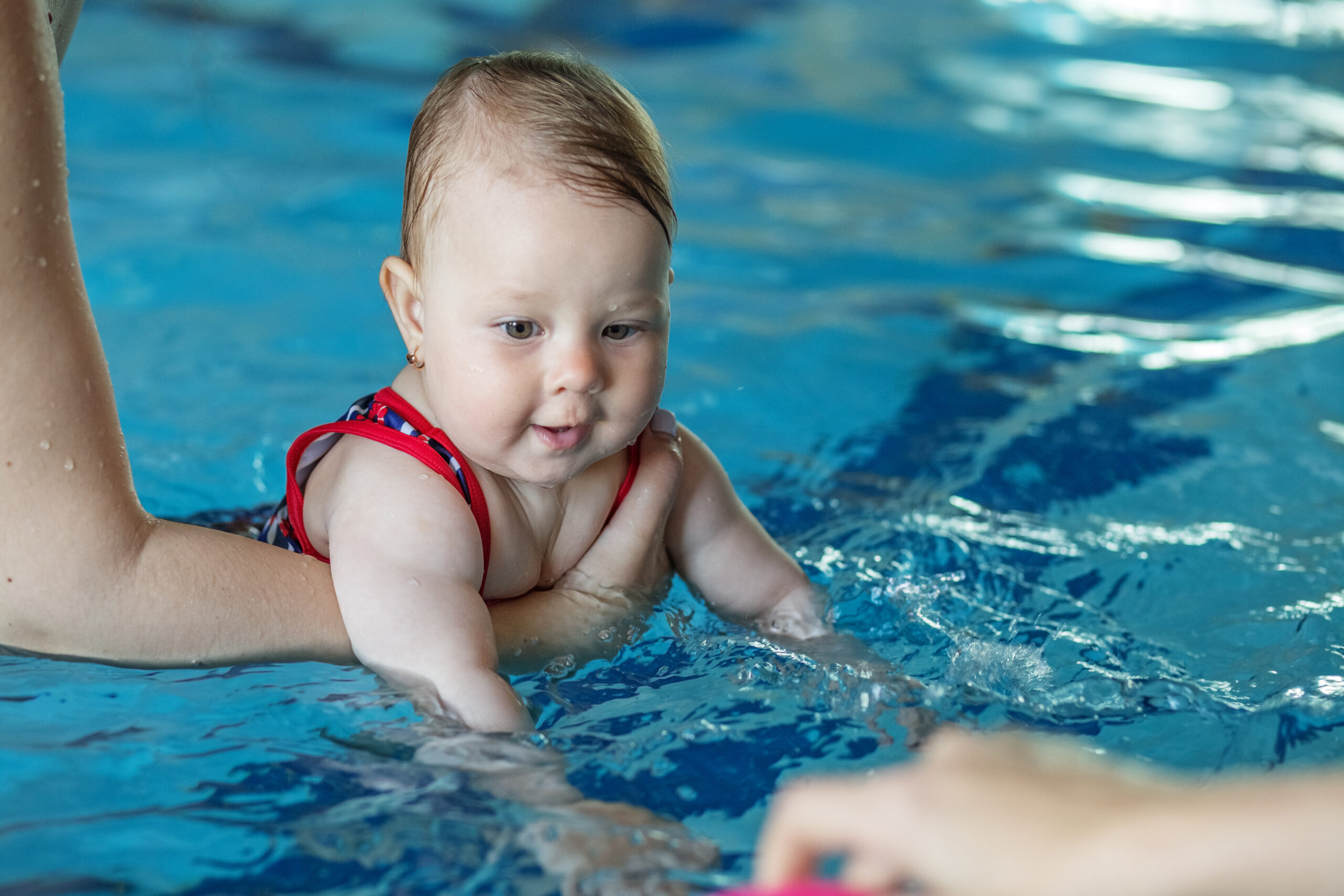 mom supports baby with hands in swimming pool tea 2022 06 02 06 01 01 utc scaled